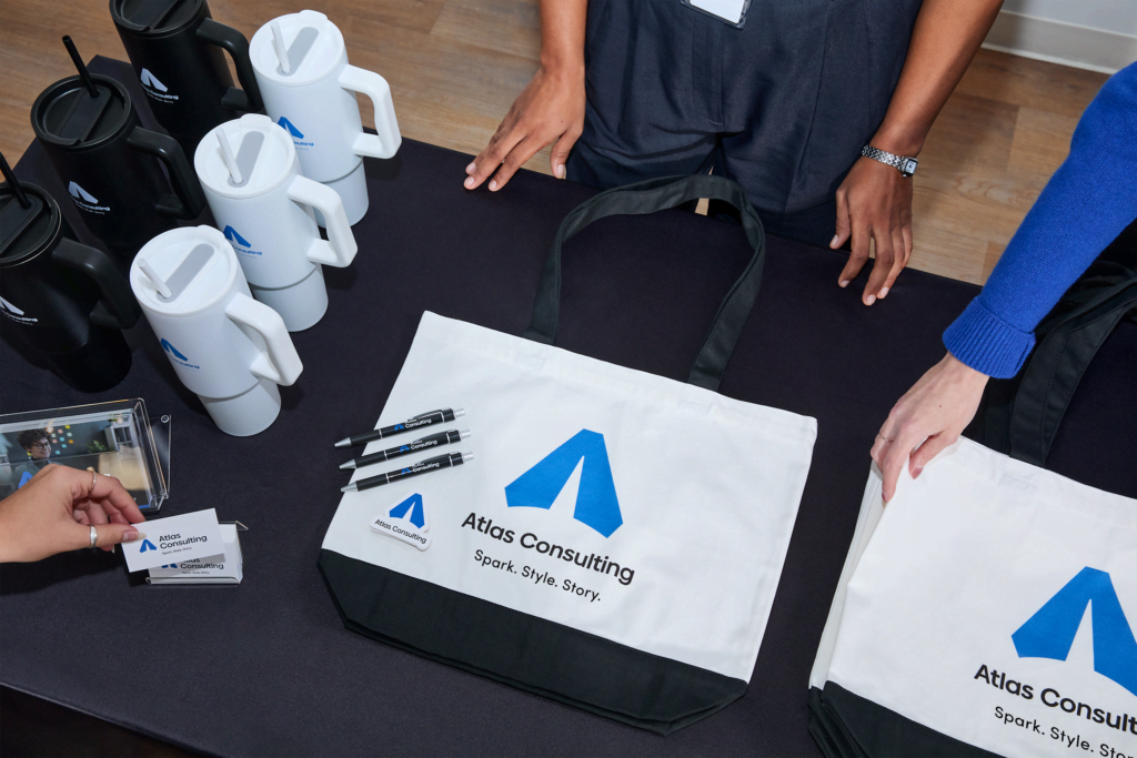 Branded tote bags, mugs, and pens displayed on a table at a trade show booth